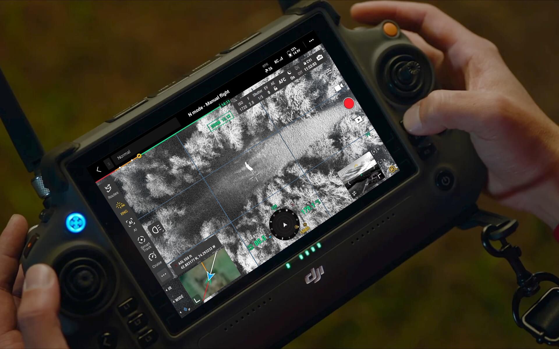 Person holding a drone controller with a live infrared image display showing terrain and controls on the screen.