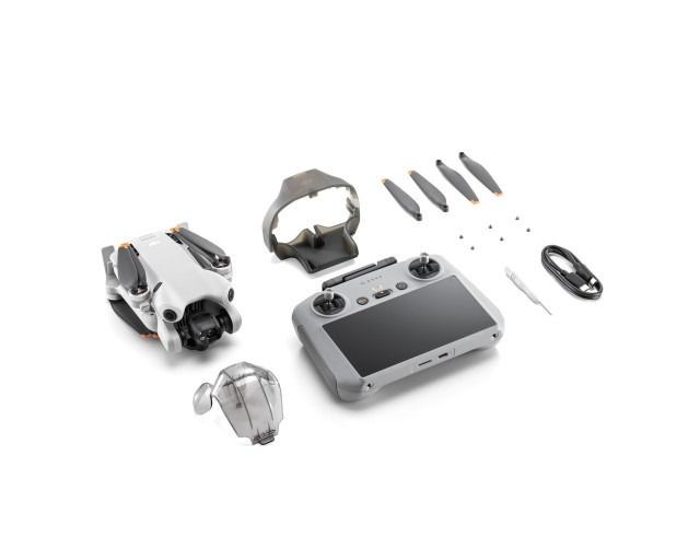 Drone kit with remote controller, propellers, and accessories arranged on a white surface.