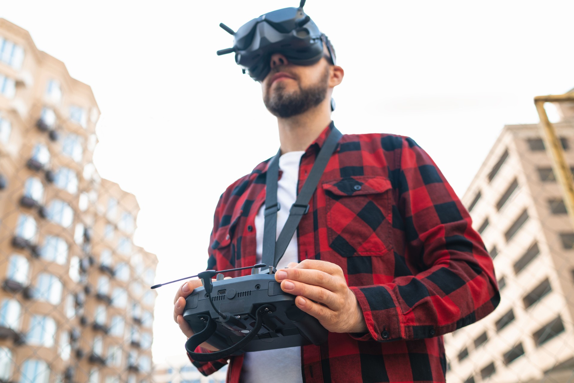 Close up outdoor portrait of a male professional fpv drone pilot wearing goggles and using remote controller to operate multicopter at the street